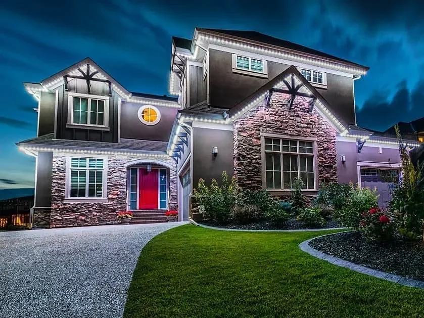 Three-storey stone-front home at dusk with permanent lights along every roofline